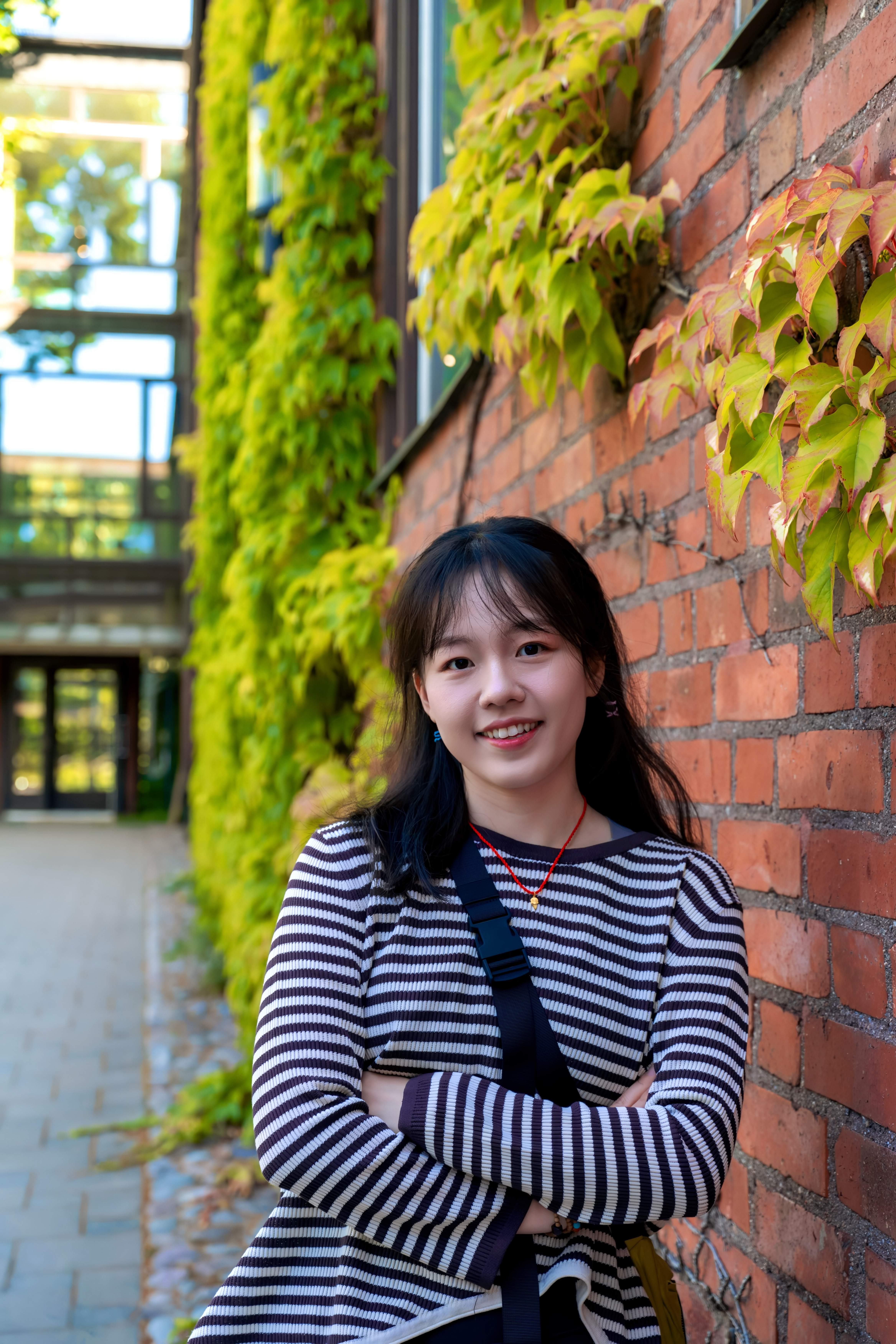 Portrait of Jingyi Mao by a brick wall covered with green leaves